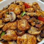 "Tender Pieces of Chicken Stir-Fried with Sliced Mushrooms, Coated in a Glossy Black Pepper Sauce, Garnished with Fresh Green Onions, and Served in a Steaming Hot Wok."