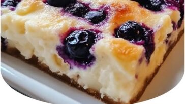 A slice of Blueberry Cottage Cheese Breakfast Bake with a golden-brown crust and fresh blueberries scattered on top, showcasing its creamy texture and vibrant color.