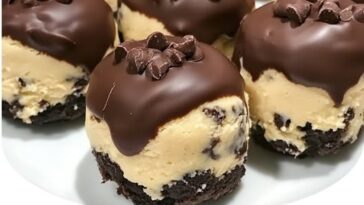 A close-up of chocolate chip cookie dough brownie bites stacked on a plate, with gooey chocolate chips visible and a rich, fudgy texture.