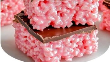 Chocolate-covered Rice Krispies treats with a cherry center, drizzled with a layer of rich chocolate, creating a glossy finish. Each square is topped with a bright red maraschino cherry, adding a pop of color and flavor.
