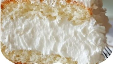 A slice of Coconut Cloud Cake topped with coconut flakes, showcasing its fluffy, creamy texture with a light, airy crumb.