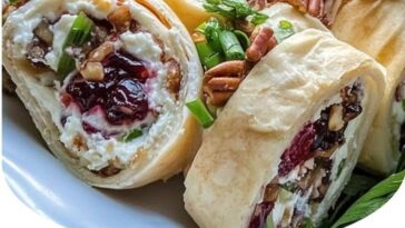 "Festive cranberry and feta cream cheese roll-ups with a swirl of red cranberries and white feta, wrapped in a tortilla, sliced into bite-sized pieces, and served on a platter."