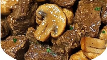 "Tender beef tips and mushrooms simmering in a creamy sauce, served in a crockpot with herbs and spices."