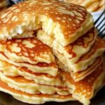 "Fluffy, golden flourless cottage cheese pancakes stacked on a plate, topped with fresh fruit and a drizzle of syrup."