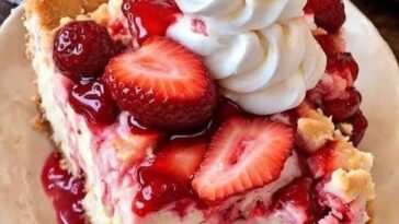 A warm, golden-brown strawberry cheesecake dump cake with a crumbly top, revealing layers of sweetened cream cheese, strawberry filling, and a buttery cake mix. The dish is garnished with fresh strawberries for a vibrant touch.