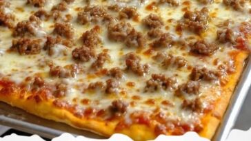 A slice of classic school pizza with a crispy golden crust, topped with tomato sauce, melted cheese, and a sprinkle of herbs, placed on a paper tray.