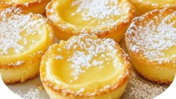 Mini lemon impossible pies in small ramekins with a golden crust and lemon filling, garnished with a sprinkle of powdered sugar.