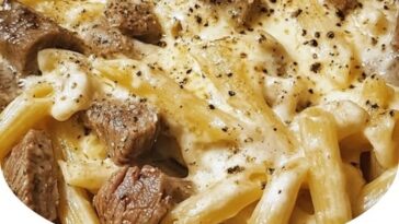 A plate of creamy ranch steak and mozzarella garlic butter pasta, with tender steak slices on top of a bed of creamy pasta, garnished with herbs and melted mozzarella cheese.