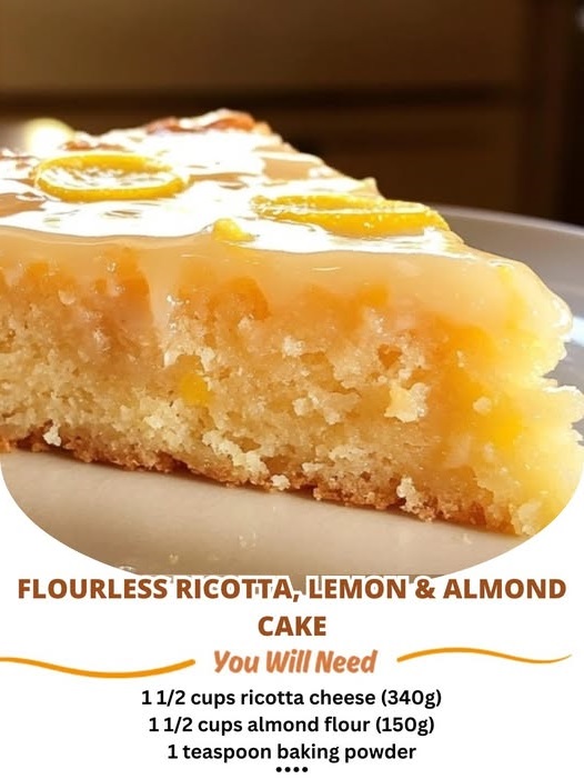 A slice of flourless ricotta, lemon, and almond cake on a white plate, topped with powdered sugar and a lemon zest garnish.