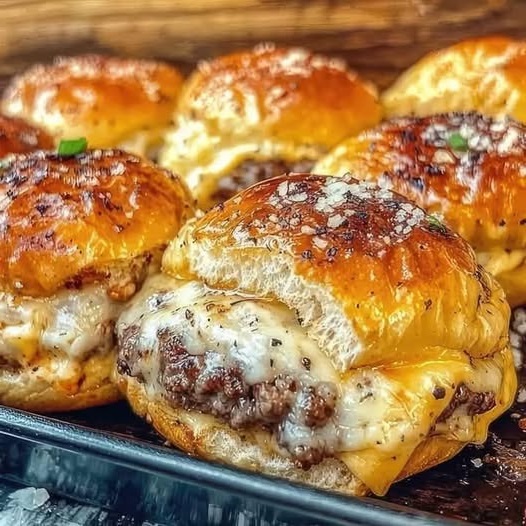 A plate of garlic parmesan cheeseburger bombs, golden brown and stuffed with melted cheese and seasoned beef, garnished with fresh parsley.