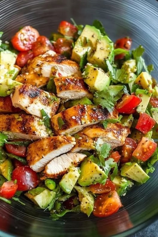 A fresh Grilled Chicken Avocado Salad with grilled chicken slices, creamy avocado, mixed greens, and vibrant vegetables, drizzled with a zesty dressing.