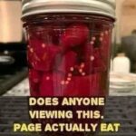 A jar of vibrant red pickled beets alongside a bowl of fresh, sliced beets and a variety of spices used for pickling, including garlic, dill, and peppercorns.