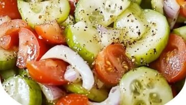 A fresh bowl of marinated cucumber, onion, and tomato salad, featuring vibrant, sliced vegetables soaked in a tangy vinaigrette, garnished with fresh herbs.