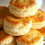 Fluffy, golden-brown buttermilk biscuits stacked on a plate with a pat of butter melting on top