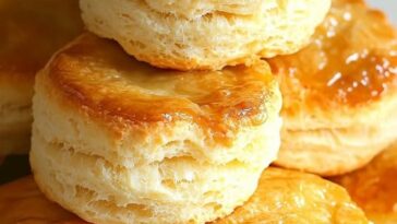 Fluffy, golden-brown buttermilk biscuits stacked on a plate with a pat of butter melting on top