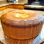 A slice of golden, perfectly baked Million Dollar Pound Cake with a smooth, buttery texture, served on a white plate with a light dusting of powdered sugar.