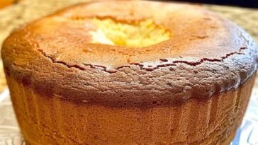 A slice of golden, perfectly baked Million Dollar Pound Cake with a smooth, buttery texture, served on a white plate with a light dusting of powdered sugar.