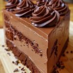 A decadent slice of no-bake chocolate mousse cake, topped with a drizzle of chocolate ganache and a dusting of cocoa powder, served on a plate.
