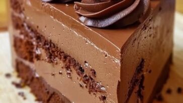 A decadent slice of no-bake chocolate mousse cake, topped with a drizzle of chocolate ganache and a dusting of cocoa powder, served on a plate.