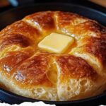 A golden, fluffy loaf of stovetop bread, sliced and displayed on a wooden cutting board, with a light, airy texture visible inside.