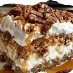 A slice of pecan pie lasagna with layers of creamy filling, pecans, and a golden crust, topped with whipped cream.