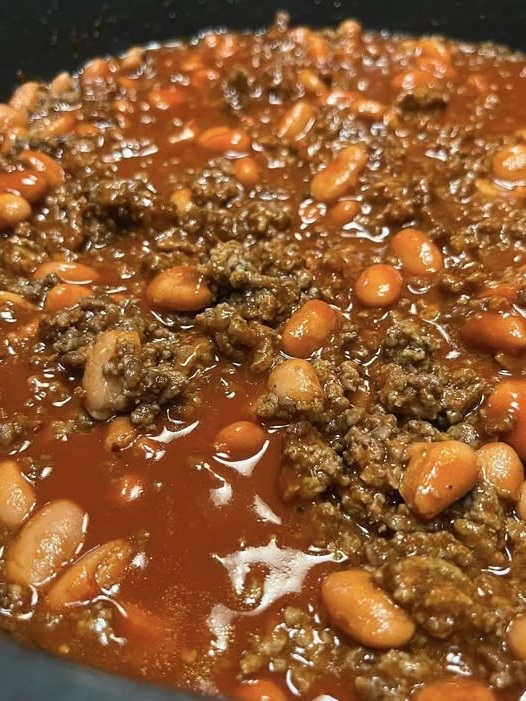 Hearty pinto bean chili served in a bowl, topped with shredded cheese, sour cream, and fresh cilantro, with a side of cornbread.