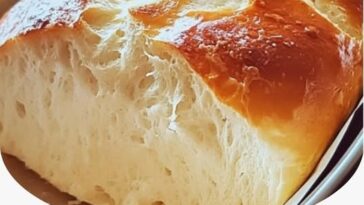 freshly baked loaf of homemade bread with a golden brown crust, sliced to reveal its soft, fluffy interior, served on a wooden cutting board.