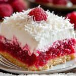 A slice of Raspberry Zinger Poke Cake, with vibrant raspberry filling soaked into the cake, topped with fluffy white frosting and fresh raspberries, served on a decorative plate.