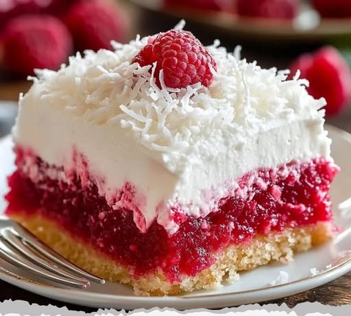 A slice of Raspberry Zinger Poke Cake, with vibrant raspberry filling soaked into the cake, topped with fluffy white frosting and fresh raspberries, served on a decorative plate.