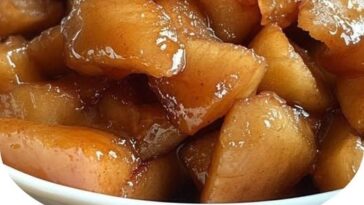 A bowl of Slow Cooker Cracker Barrel Fried Apples, caramelized with cinnamon and sugar, garnished with a sprinkle of cinnamon, served with a spoon, exuding a warm, comforting aroma.