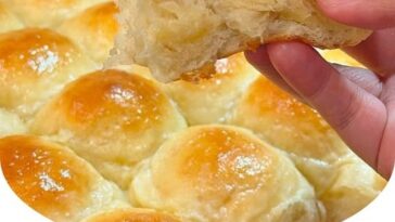 A batch of soft and buttery homemade rolls, golden brown on the outside with a light, fluffy interior, served warm on a rustic wooden table.