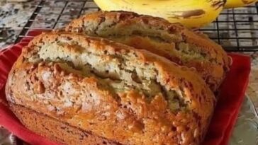 Slice of soft and moist banana bread on a wooden cutting board with a few ripe bananas beside it