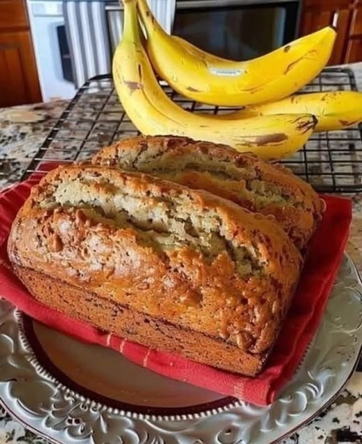 Slice of soft and moist banana bread on a wooden cutting board with a few ripe bananas beside it