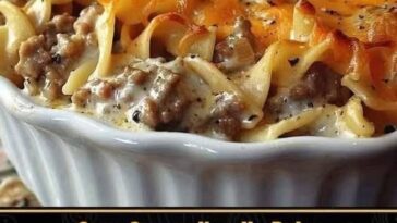 A baked dish of sour cream noodle bake with creamy layers of pasta, ground meat, and cheese, topped with a golden-brown crust.
