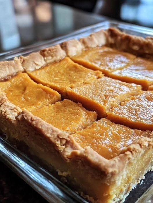 A plate of Sweet Potato Pie Bars with a golden-brown crust and a smooth, spiced sweet potato filling, topped with a dusting of cinnamon.