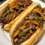 A Philly-style steak and pepper hoagie sandwich with thinly sliced steak, sautéed peppers and onions, melted cheese, all nestled in a toasted hoagie roll.