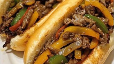 A Philly-style steak and pepper hoagie sandwich with thinly sliced steak, sautéed peppers and onions, melted cheese, all nestled in a toasted hoagie roll.