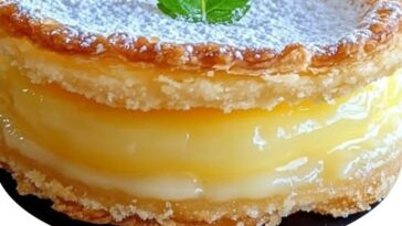 Mini lemon impossible pies on a white plate, topped with powdered sugar and lemon zest.