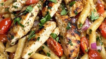 bowl of pasta topped with grilled chicken, fresh tomatoes, basil, and drizzled with balsamic glaze.