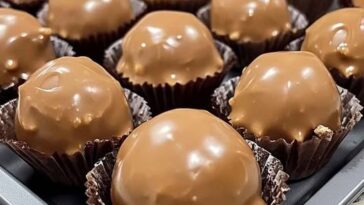 Close-up of homemade Butterfinger Balls arranged on a tray, coated in chocolate with a crunchy, peanut-buttery texture inside.