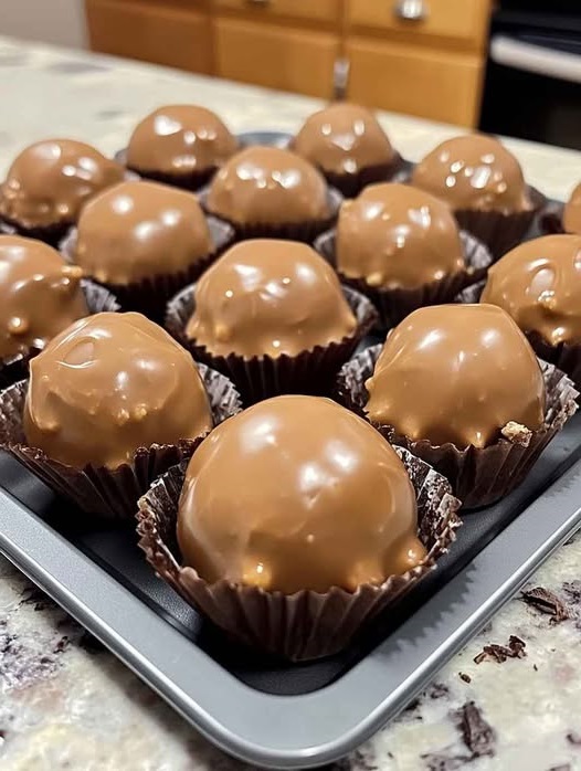 Close-up of homemade Butterfinger Balls arranged on a tray, coated in chocolate with a crunchy, peanut-buttery texture inside.