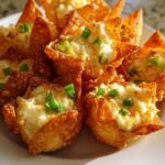 Golden-brown crab Rangoon bombs with a crispy exterior, garnished with chopped green onions and served with a side of dipping sauce.