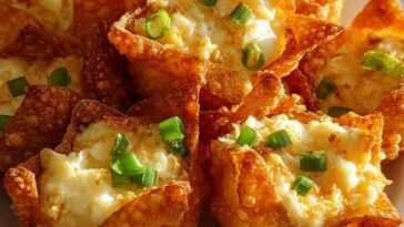 Golden-brown crab Rangoon bombs with a crispy exterior, garnished with chopped green onions and served with a side of dipping sauce.