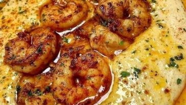 A bowl of creamy grits topped with Cajun-seasoned shrimp, garnished with chopped green onions and a sprinkle of paprika, served with a drizzle of butter sauce.