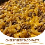 Cheesy beef taco pasta in a skillet, topped with melted cheese and garnished with fresh herbs.