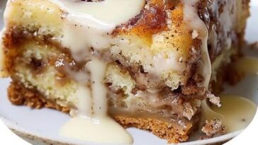 A slice of cinnamon roll cake with swirls of cinnamon filling and a drizzle of icing on top, served on a plate.