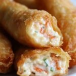 Golden, crispy egg rolls stuffed with a creamy crab filling, served with a dipping sauce on the side.