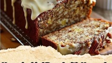 A moist slice of banana bread topped with thick cream cheese frosting and garnished with toasted coconut and pineapple pieces.
