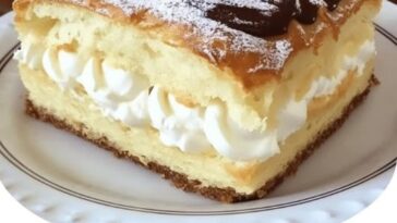 A slice of cream puff cake with a light, fluffy texture, topped with creamy filling and a drizzle of chocolate.