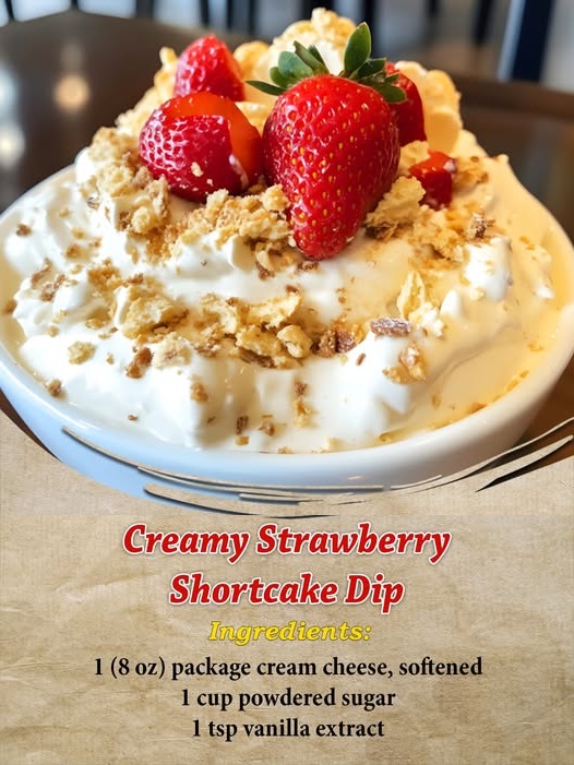 Bowl of creamy strawberry shortcake dip topped with crushed golden cookies and fresh strawberry slices, surrounded by dippers like vanilla wafers and graham crackers.